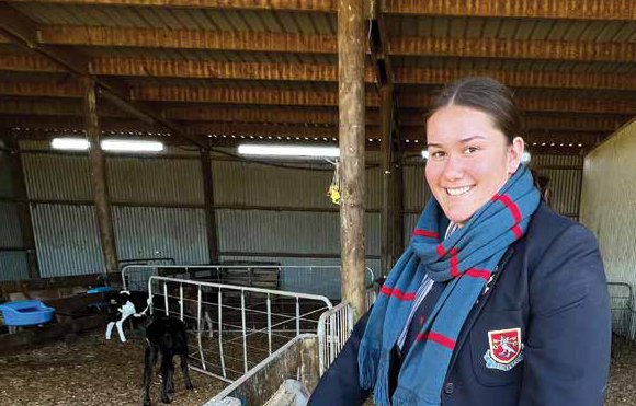 Bex Watson from St Peter's standing in front of some calves in a barn